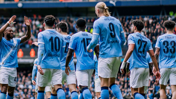 Manchester City football players in team kit celebrating on the field, featuring player numbers and names on their backs.