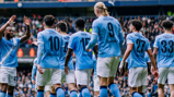 Manchester City football players in team kit celebrating on the field, featuring player numbers and names on their backs.