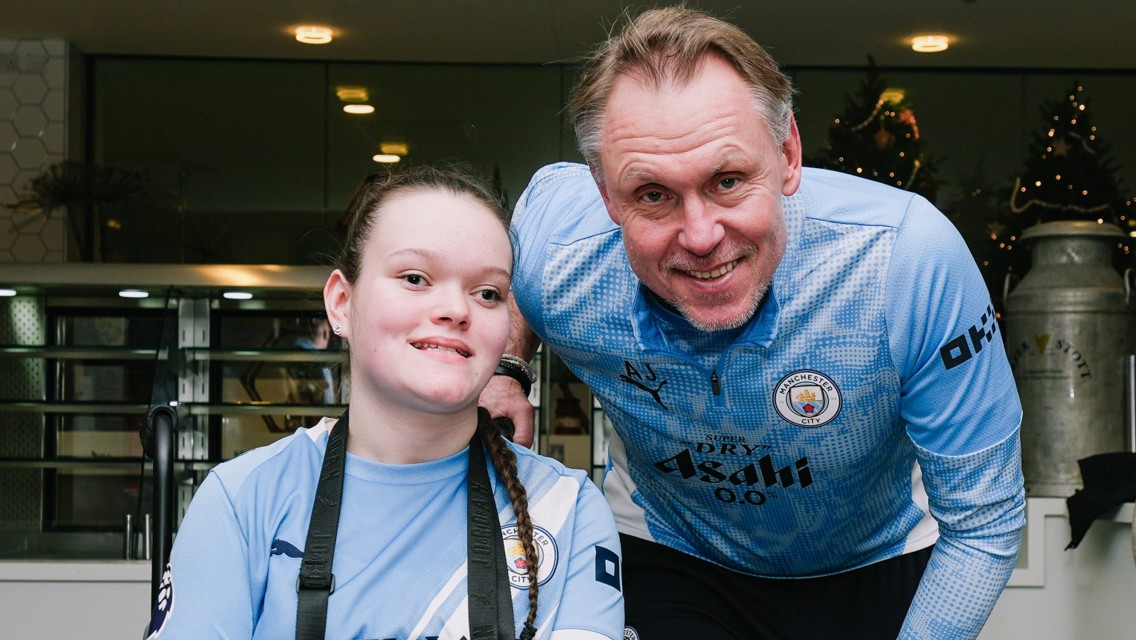 Two people wearing Manchester City gear pose for a photo in a setting with Christmas decorations.