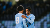 Two Manchester City players in blue jerseys with the number 8 visible on one, embracing on the field during a match.