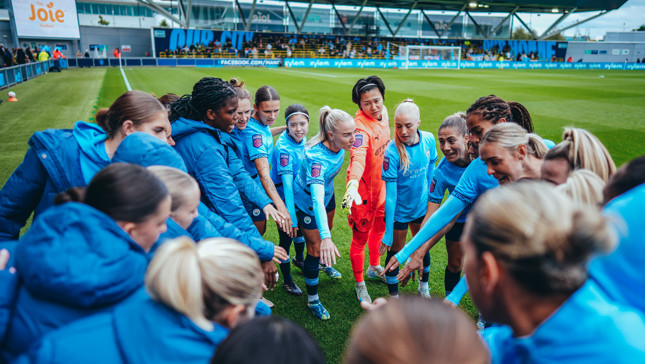 Manchester City Women's Team huddled during a pre-match talk at Joie Stadium with visible Manchester City logos on their kits.