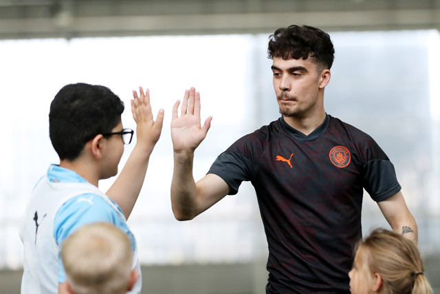 A Manchester City player giving a high five to a young boy during a training session at the indoor facility.