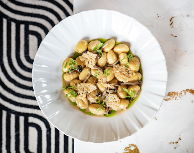 A plate of gnocchi served with mushrooms, Parmesan crisps, and fresh herbs.