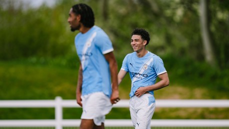 Two football players wearing Manchester City training kits on a grassy field.
