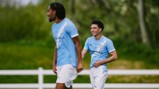 Two football players wearing Manchester City training kits on a grassy field.