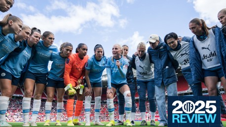 A group of Manchester City Women's football team players in a huddle on the field, wearing blue jerseys and training gear, with a '2025 Review' graphic on the side.