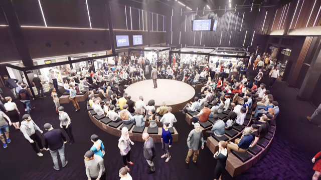 Large crowd seated around a circular stage at an indoor expo event with vendor booths visible in the background.