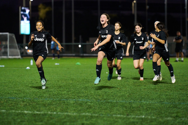 Five female soccer players wearing Juventus kits training on a grass field at night.