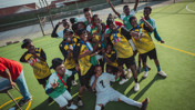A group of young soccer players wearing medals and uniforms celebrate with a trophy on a sports field.
