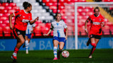 A women's football match featuring Manchester City wearing white and blue uniforms against Charlton Athletic in red, in a stadium with red and white seating.