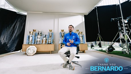 A person sits in a chair surrounded by football trophies, including Premier League and UEFA Champions League trophies. The text reads 'Thank You Bernardo' with years 2017 to 2026.