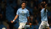 Two football players in a Manchester City kit celebrating on the field. Player number 10 is visible in the image.