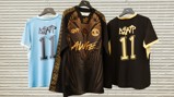 Three Puma jerseys on hangers: a light blue, a black with gold accents, and a black with intricate gold designs featuring the term 'AWGE' and a stylized number '11'.