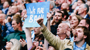 A crowd of enthusiastic fans, with one holding up a sign that reads 'WE ARE BACK'.