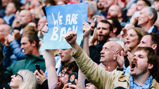 A crowd of enthusiastic fans, with one holding up a sign that reads 'WE ARE BACK'.