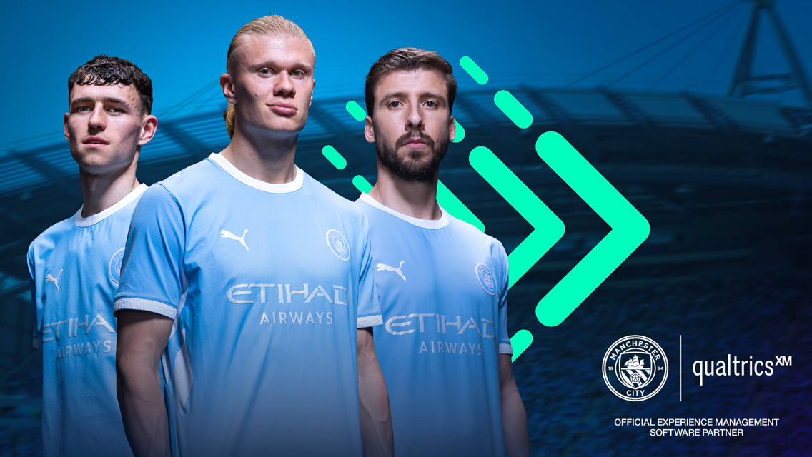 Three Manchester City players wearing the team's kit in front of a stadium background with Manchester City and Qualtrics logos.