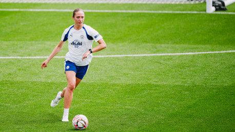A Manchester City Women's team player in training, wearing a white and blue kit with Puma branding and playing on a grass field.
