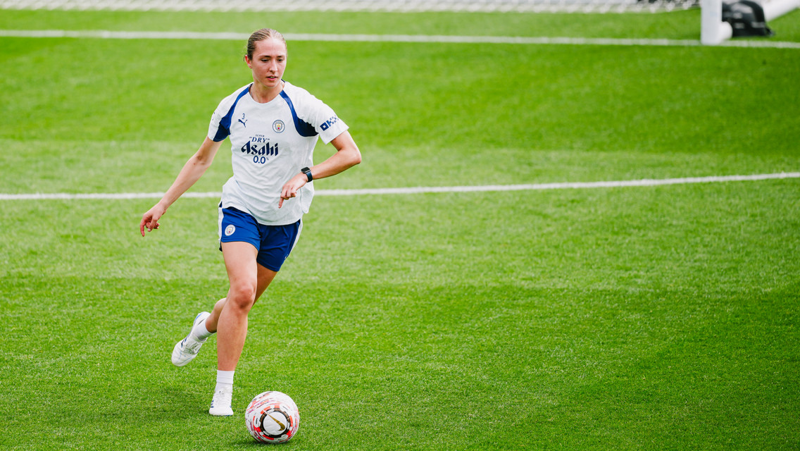 A Manchester City Women's team player in training, wearing a white and blue kit with Puma branding and playing on a grass field.