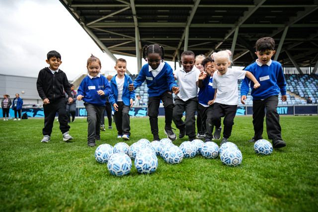 A group of children, all dressed in blue and white uniforms, are playing with multiple soccer balls on a field.
