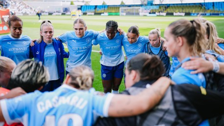 Manchester City women's team huddle wearing Etihad Airways branded sportswear on the field.