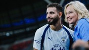 A male football player wearing a Manchester City jersey poses with a female fan at a stadium.