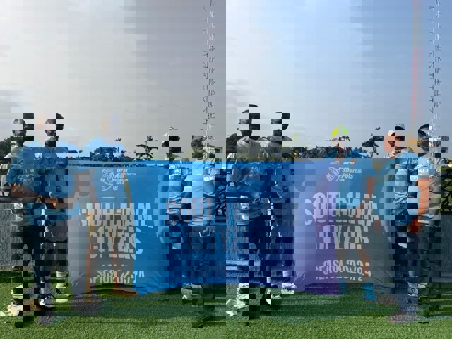 Four people in Manchester City jerseys holding a banner that reads 'South Ghana Cityzens Official Supporters Club Season 2023/24'.