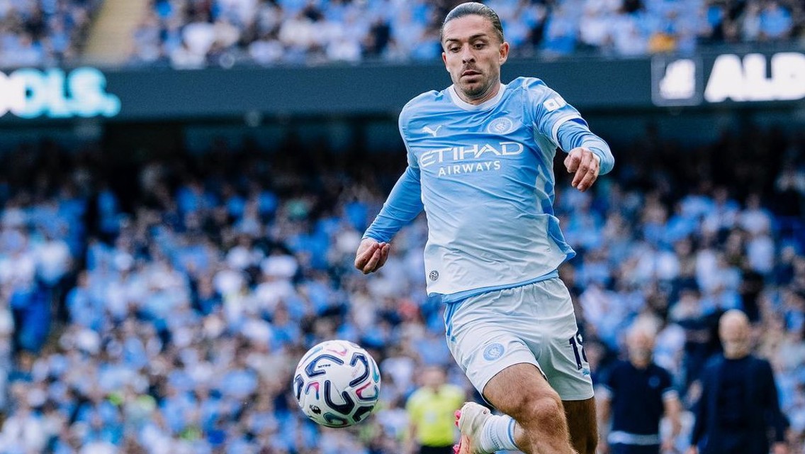 A football player in a Manchester City kit attempting to control the ball in a stadium full of spectators.
