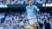 A football player in a Manchester City kit attempting to control the ball in a stadium full of spectators.