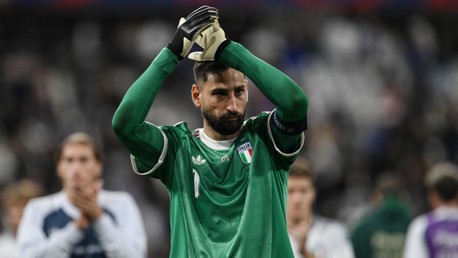 A goalkeeper in a green Italy jersey claps with gloved hands during a football match.