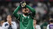 A goalkeeper in a green Italy jersey claps with gloved hands during a football match.