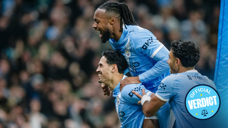 Manchester City players wearing light blue jerseys celebrate a goal during a match. The jersey features the Manchester City crest.