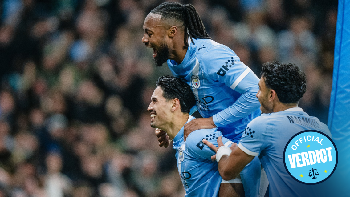 Manchester City players wearing light blue jerseys celebrate a goal during a match. The jersey features the Manchester City crest.