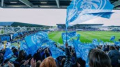 Fans waving Manchester City flags during a match at the Academy Stadium.
