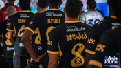 Football team wearing black and gold jerseys with player names in a tunnel. The jerseys promote experience Abu Dhabi. Asia Tour '26 mentioned in the corner.