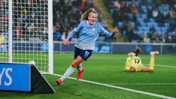 A soccer player from Manchester City Women's team celebrates a goal during a match, wearing a light blue jersey with the number 11. The goalkeeper is visible on the ground in the background.