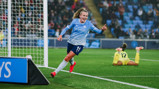 A soccer player from Manchester City Women's team celebrates a goal during a match, wearing a light blue jersey with the number 11. The goalkeeper is visible on the ground in the background.