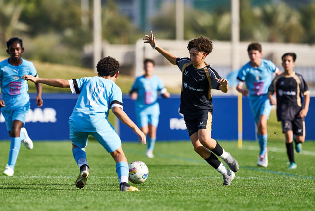 Children playing a soccer match; teams in black and light blue uniforms competing on the field.