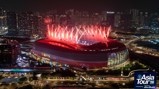 A stadium illuminated with fireworks and lights during the Asia Tour '26 event presented by Abu Dhabi. The surrounding city at night provides a vibrant backdrop.