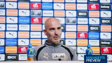 A man speaking at a press conference, wearing a Manchester City jacket, with sponsor logos in the background.