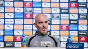 A man speaking at a press conference, wearing a Manchester City jacket, with sponsor logos in the background.