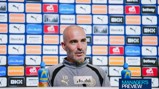 A man speaking at a press conference, wearing a Manchester City jacket, with sponsor logos in the background.