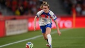 A female soccer player in an England jersey, number 11, dribbles the ball during a match. The uniform features blue shorts and socks with a white jersey and logos.