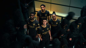 Four individuals wearing Manchester City's 2023 kit featuring Puma and Etihad Airways branding, surrounded by others in dark hoodies.