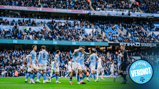 Manchester City players celebrating a goal at Etihad Stadium with a referee nearby, in front of a large crowd.