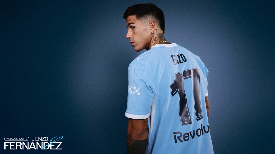 A man wearing a light blue soccer jersey with the name 'ENZO' and number '17'. The jersey features Puma and Revolut branding. The text reads 'Welcome to City Enzo Fernandez'.