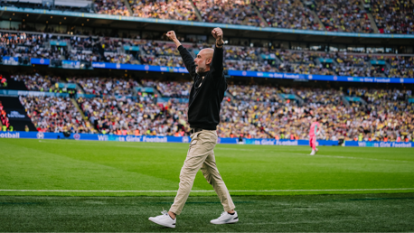 Person with raised arms on a football field with a packed stadium in the background.