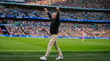 Person with raised arms on a football field with a packed stadium in the background.