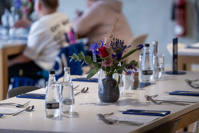 Table with a floral centerpiece, bottles of water, and cutlery. People blurred in the background.