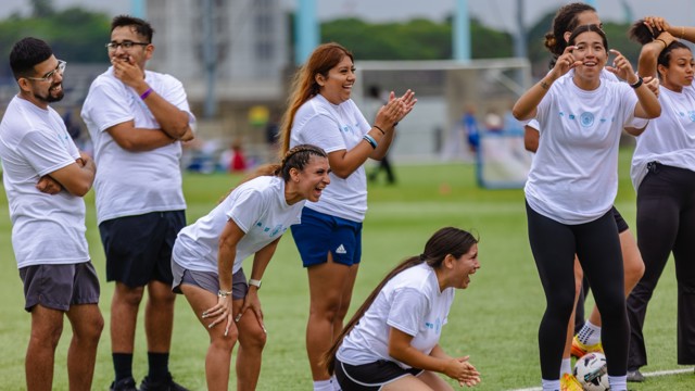 A group of people in white shirts enthusiastically cheering on a soccer field.