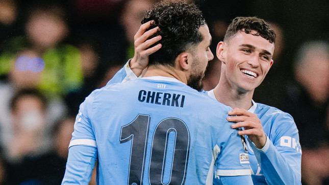 Two soccer players from Manchester City in light blue jerseys are celebrating. One player is labeled 'CHERKI' with number 10.